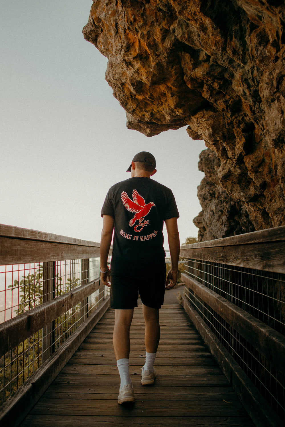 Person walking on a wooden path towards a large rock formation